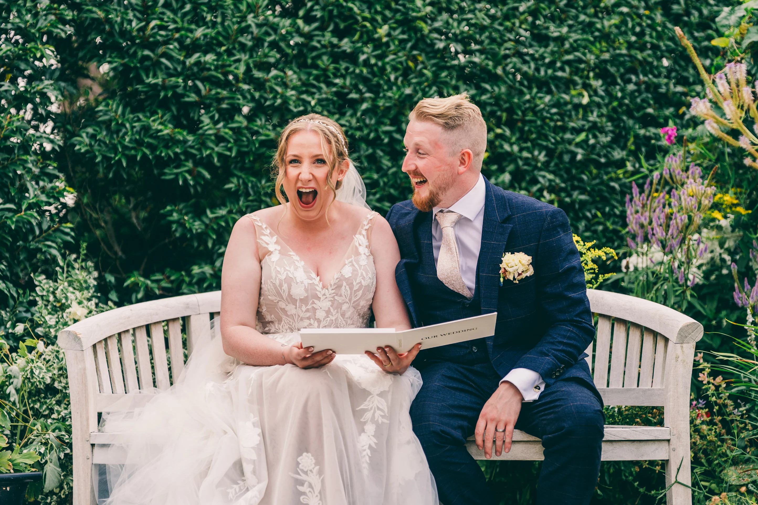 A newlywed couple laughing together while watching their wedding film